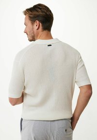 Polo bianco a maniche corte in cotone lavorato a maglia con colletto a costine e accenti laterali. Tessuto testurizzato e traspirante con gancio sul retro del collo.