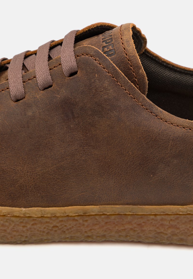 Brown leather shoe with brown laces, featuring a smooth texture and stitched accents. Rubber sole with a textured surface for grip.