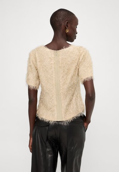 Top beige testurizzato con maniche corte, caratterizzato da una finitura pelosa e una chiusura con zip sul retro. Abbinato a pantaloni in pelle nera.