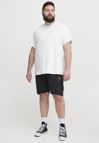 White cotton t-shirt paired with black shorts featuring a small gold graphic. Black high-top sneakers and white crew socks complete the look.