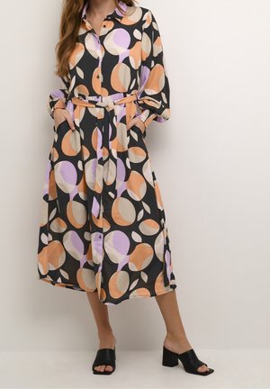Robe chemise en tissu noir avec de grands cercles abstraits en orange, violet et beige. Comprend une ceinture et des poches latérales.