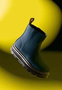 Blue ankle boot made of textured material, featuring a black elastic band, yellow stitching, and a rugged black sole with deep treads.