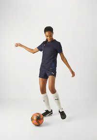 Tumesinise värvi sportlik särk ja püksid PUMA logoga, valged põlvikud, mustad ketsid ja oranž-hall jalgpall.