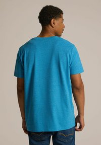 Koszulka z krótkim rękawem z niebieskiego melanżowego materiału, okrągły dekolt, luźny fason, w połączeniu z dżinsami, widok z tyłu.