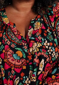 Blusa con motivo floreale dai colori vivaci, tra cui rosa, arancione e verde, realizzata in tessuto leggero, con scollo a v e dettagli con bottoni.