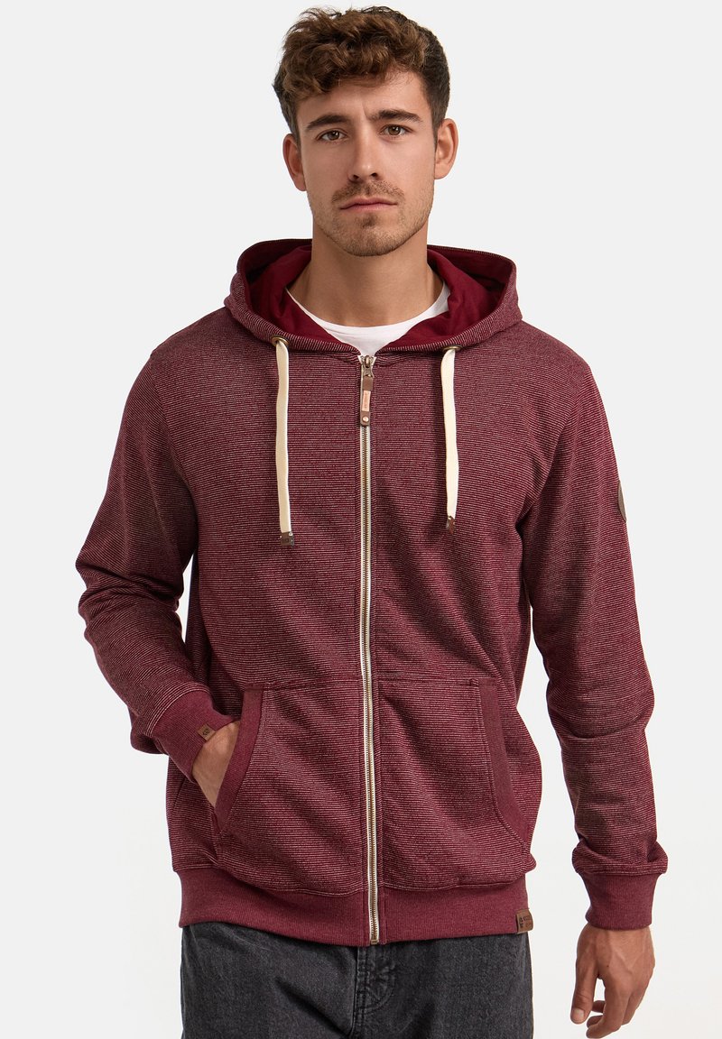 Bordeauxfarbene Zip-Hoodie mit Kordelzugkapuze, Fronttaschen, gerippten Bündchen und einer strukturierten Oberfläche. Mit einem kleinen Logo-Patch am Ärmel.