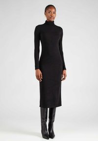 Zwarte coltrui jurk in een slimfit ontwerp, gemaakt van een gestructureerde breisel stof. Draag met kniehoge glanzende zwarte laarzen.