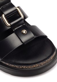 Sandal in pelle nera con ampie cinghie, hardware in oro, soletta in sughero testurizzato e suola chunky nera.