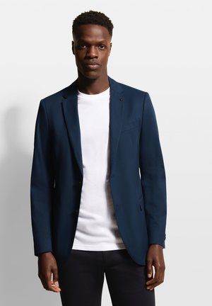 Marineblauer Blazer mit Reverskragen, einreihigem Knopfverschluss, zwei vorderen Taschen und glatter Textur, über einem weißen T-Shirt getragen.