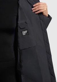 Czarna pikowana kurtka o matowym wykończeniu, z kieszenią na rękawie i zapięciem na zamek, wykonana z miękkiego, lekkiego materiału.