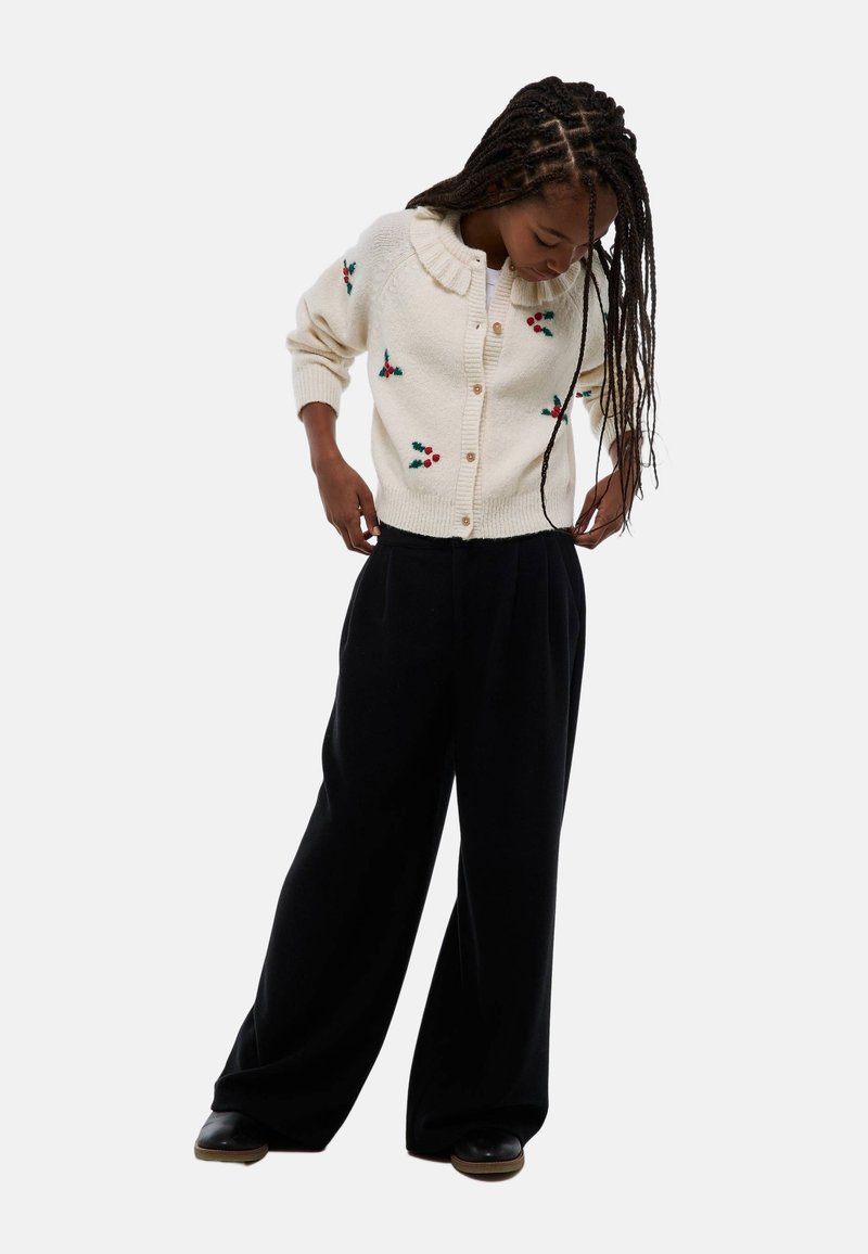 Cardigan crème avec broderie florale, col côtelé et boutons, associé à un pantalon noir à jambes larges. Texture lisse, coupe décontractée.