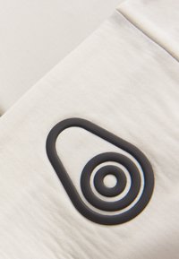 Vitt tyg med en slät textur har en framträdande svart gummilogga i oval form med koncentriska cirklar.