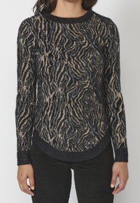 Suéter de patrón negro y beige con un acabado texturizado y suave, que presenta un cuello redondo y un dobladillo curvado. Mangas largas y puños ajustados.