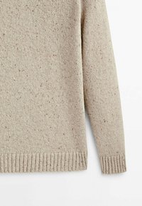 Pull en tricot beige avec motif moucheté, ourlet et poignets côtelés, présenté sur un fond blanc.