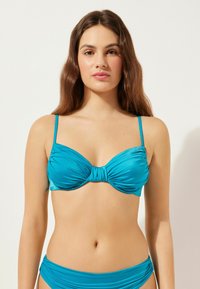 Tyrkis bikiniöverdel med en vriden frondesign och tunna justerbara remmar. Slät struktur med en åtsittande silhuett och inga hårdvarudetaljer.