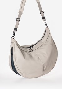 Beige Schultertasche mit geschwungener Form, aus glattem Material gefertigt. Verfügt über schwarze Reißverschlusstaschen und einen verstellbaren Riemen mit Hardware-Akzenten.