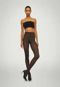 Leggings neri in tessuto trasparente caratterizzati da un design a vita alta, una texture liscia e una silhouette aderente, abbinati a tacchi alti neri e a un top bandeau.