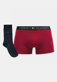 Røde ternede boxershorts med en marineblå taljebånd med "TOMMY HILFIGER" i guld. Et sort sok med et lille logo medfølger.