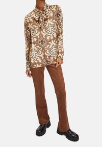 Långärmad blus med blommönster i bruna, krämiga och rostiga nyanser, ihopparad med bruna kordfläskbyxor och blanka svarta platåstövlar.