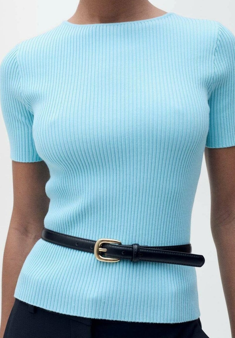 Haut à manches courtes côtelé bleu clair associé à une ceinture en cuir noir avec une boucle dorée, porté avec un pantalon foncé.