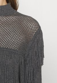 Gros plan sur une personne portant un pull en maille gris foncé avec un dos supérieur en maille et des motifs de côtes texturés et de torsades.