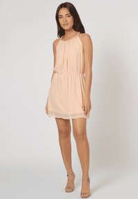 Vestido sin mangas de color durazno con un diseño plisado, cintura fruncida y detalle trenzado en el cuello. El dobladillo transparente añade suavidad al aspecto.