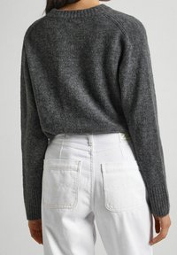 Maglione grigio lavorato a maglia con design corto e polsini a coste, abbinato a jeans bianchi a vita alta con tasche posteriori.