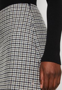 Wollrock mit einem Hahnentrittmuster in Creme, Marineblau und Hellblau, mit einer Seitennaht und einem kleinen Logo nahe dem Saum.