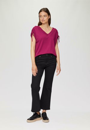 Haut fuchsia à col en V avec des détails froncés aux manches, associé à un jean noir évasé et des baskets noires avec une semelle plateforme beige.