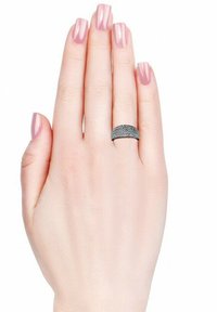 Anello nero texturizzato su una mano con unghie lunghe e rosa chiaro. L'anello presenta una banda liscia con una superficie decorata, in contrasto con il tono della pelle.