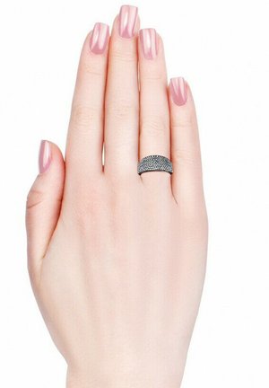 Anello nero texturizzato su una mano con unghie lunghe e rosa chiaro. L'anello presenta una banda liscia con una superficie decorata, in contrasto con il tono della pelle.