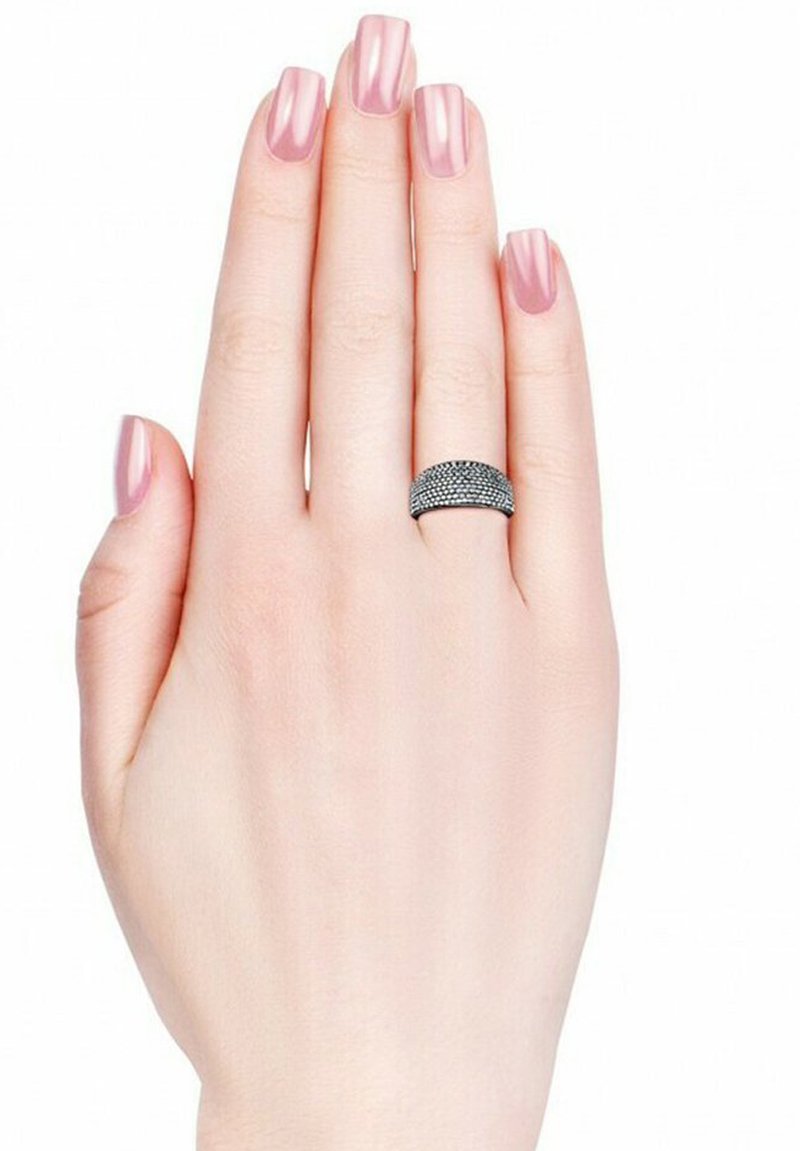 Anello nero texturizzato su una mano con unghie lunghe e rosa chiaro. L'anello presenta una banda liscia con una superficie decorata, in contrasto con il tono della pelle.