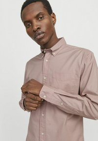 Camisa de botón de manga larga color rosa claro con un bolsillo. Presenta un collar y puños con botón, hecha de una tela suave con una textura sutil.