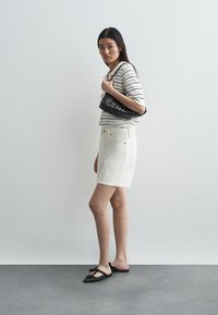 Saia de denim branca, top de malha riscada em bege e preto, bolsa preta de palha e sapatos pretos baixos. Silhueta vertical contra um fundo simples.