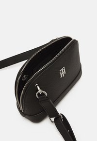 Czarna skórzana torebka na ramię o teksturowym wykończeniu, z srebrnymi suwakami i akcentem logo z przodu. W zestawie regulowany pasek.