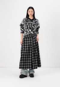 Maglione a maglia bicolore con motivo, scollatura a V, abbinato a una gonna a quadri bianca e nera a vita alta con dettagli con fibbia.