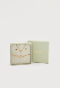 Σετ κοσμημάτων σε χρυσαφί απόχρωση σε ανοιχτό πράσινο κουτί, περιλαμβάνει κολιέ και βραχιόλι με καρδιές, με ομαλή υφή.