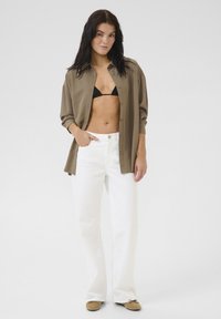 Khaki mygtukinė marškiniai, juodi bikini, balti platūs keliai ir smėliniai batai. Lygus audinys su atsipalaidavusiu siluetu, papildantis paplūdimio aprangą.