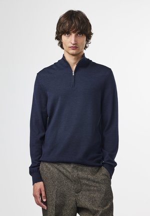 Pullover blu navy a metà zip realizzato in tessuto a maglia con polsini a coste, caratterizzato da un colletto alto e un design elegante, abbinato a pantaloni texturizzati.