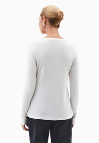 Biała koszula z długim rękawem, okrągłym dekoltem, gładką teksturą i dopasowanym krojem, zestawiona z ciemnymi dżinsami. Prosty i minimalistyczny styl.