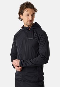Schwarze Zip-Jacke mit Kapuze, mit orangefarbenen Akzenten, schlanker Schnitt, weicher Textur und einem reflektierenden Streifen auf der Brust.