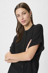 Blusa nera a maniche corte con chiusura a bottoni, scollatura arrotondata e texture morbida. Presenta una vestibilità rilassata e delicate cuciture decorative.