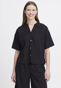 Camicia nera a maniche corte con colletto, realizzata in tessuto leggero. Presenta una chiusura frontale con bottoni e una vestibilità rilassata e ampia.
