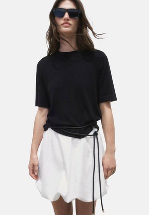 Chemise noire à manches courtes accompagnée d'une jupes blanche volumineuse, maintenue par une ceinture en corde noire. Texture lisse, design minimaliste.
