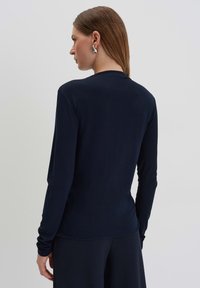 Langärmliges marineblaues Oberteil aus weicher Stoffqualität, mit Rundhalsausschnitt und schmalem Schnitt. Nahtlose Schultern und eine glatte Textur. Minimalistischer Stil.