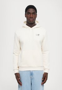 Cream-colored hoodie with a kangaroo pocket, drawstring hood, and logo on the chest; long sleeves with ribbed cuffs and hem.