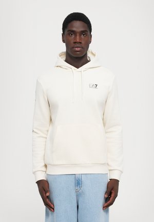 Cream-colored hoodie with a kangaroo pocket, drawstring hood, and logo on the chest; long sleeves with ribbed cuffs and hem.