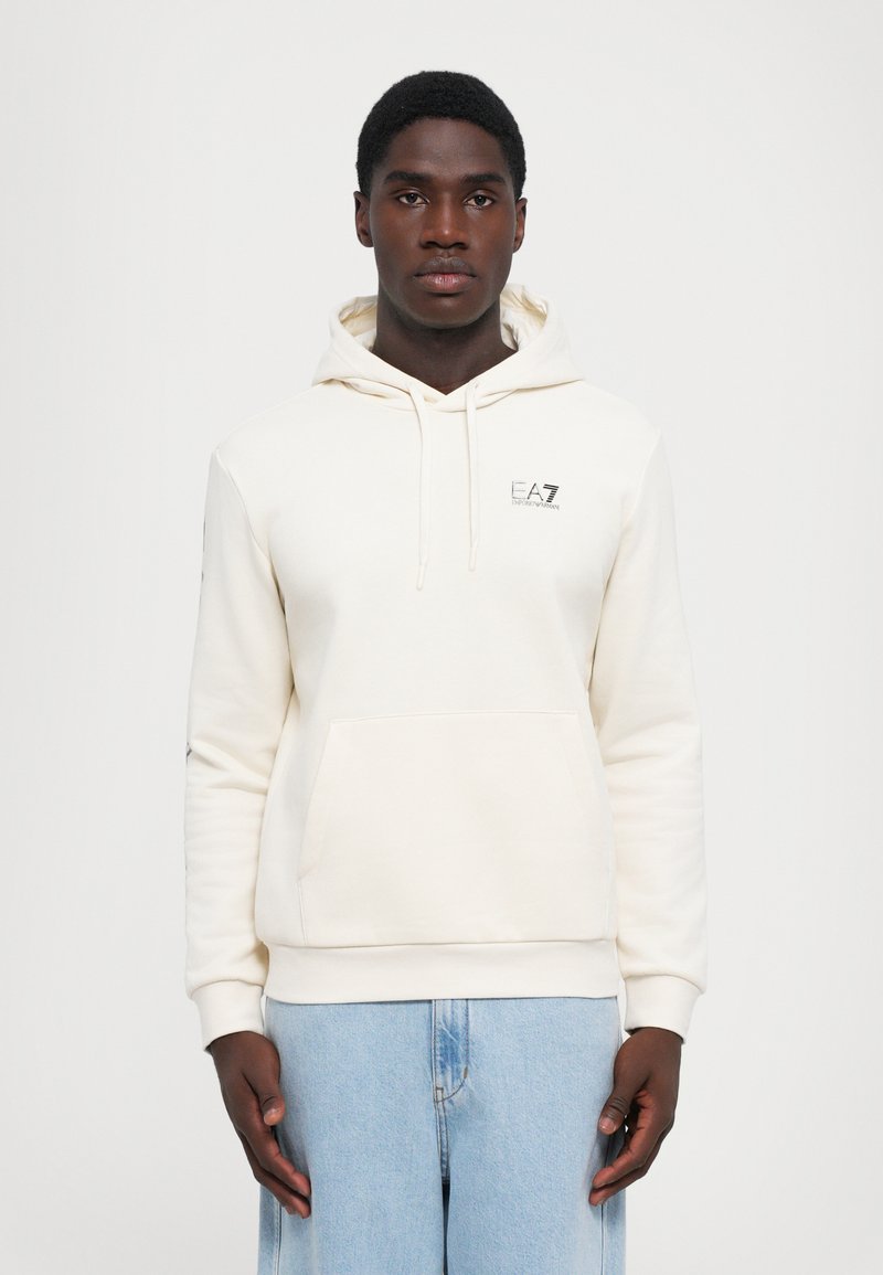 Cream-colored hoodie with a kangaroo pocket, drawstring hood, and logo on the chest; long sleeves with ribbed cuffs and hem.