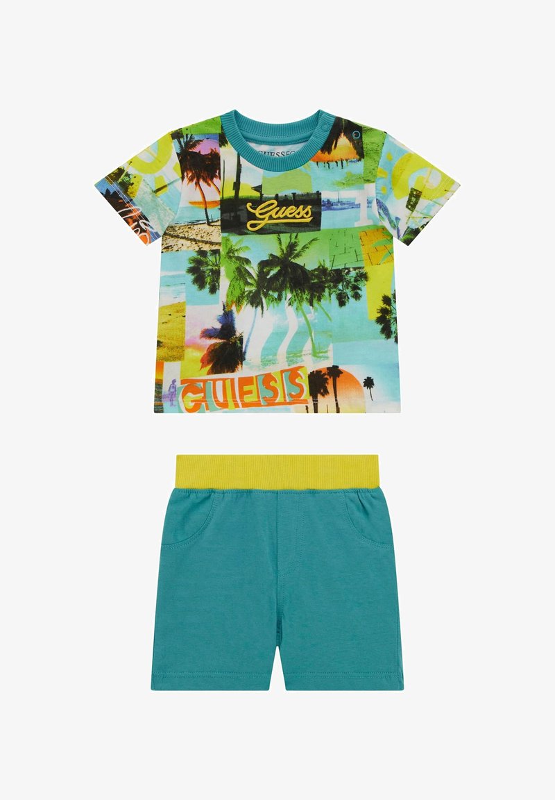 T-shirt colorato a maniche corte con stampa tropicale e logo 'Guess'; abbinato a pantaloni corti teal con una cintura elastica gialla.