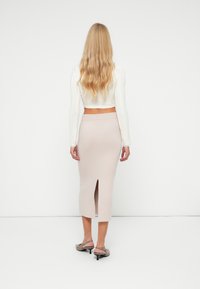 Pull en tricot blanc cropped et jupe midi beige avec une fente avant. Coupe slim, texture lisse et détails subtils. Chaussures à petit talon.